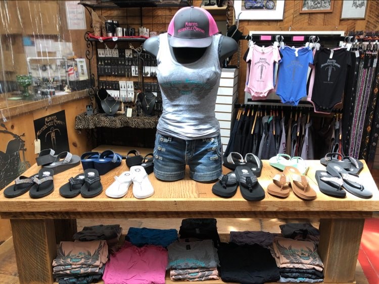 Casual footwear and motorcycle clothing display with various flip-flops and sandals on wooden shelves.